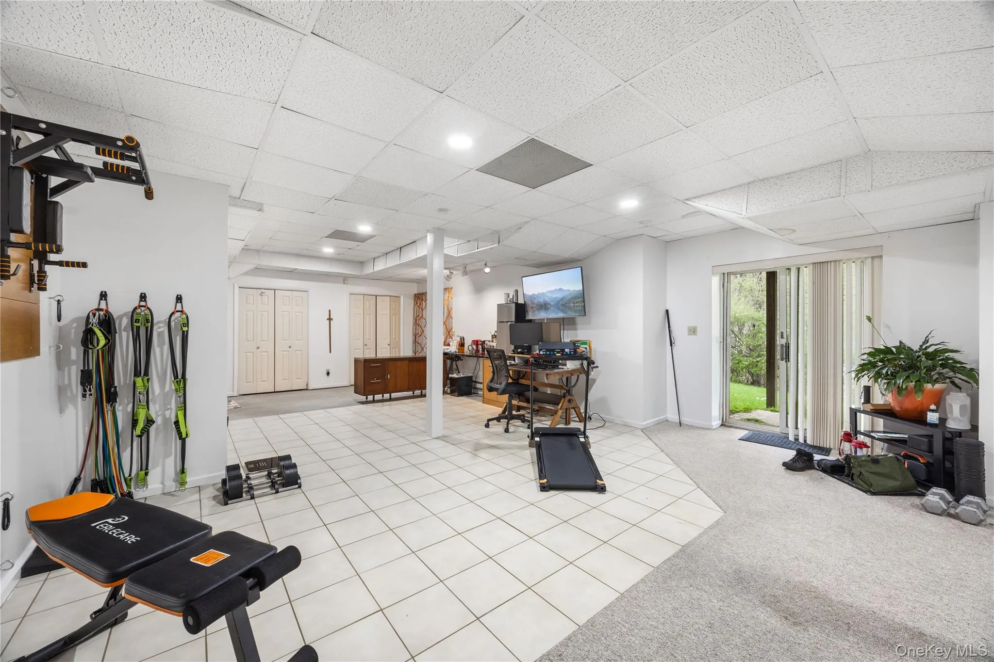 Lower level featuring a sliding glass door for outdoor access, mixed flooring with tile and carpeted areas, recessed lighting, and multiple bi-fold closet doors Lower level featuring a sliding glass door for outdoor access, mixed flooring with tile and carpeted areas, recessed lighting, and multiple bi-fold closet doors