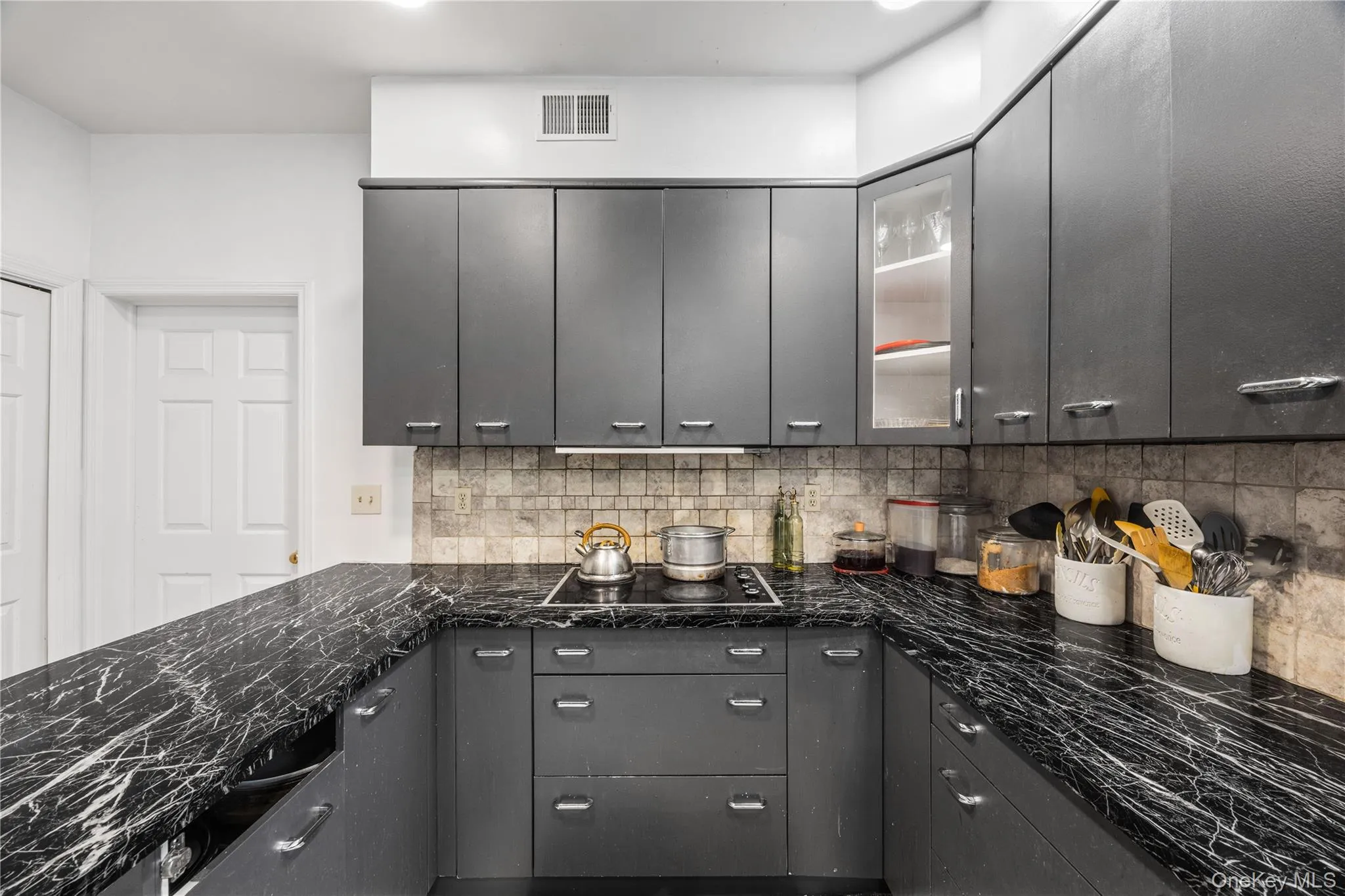 Kitchen featuring dark cabinetry, marble-finish countertops, built-in cooktop, tile backsplash, and overhead recessed lighting Kitchen featuring dark cabinetry, marble-finish countertops, built-in cooktop, tile backsplash, and overhead recessed lighting