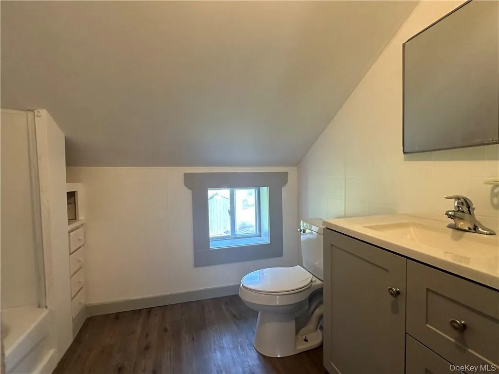 Bathroom featuring a bath, hardwood / wood-style flooring, vaulted ceiling, vanity, and toilet Bathroom featuring a bath, hardwood / wood-style flooring, vaulted ceiling, vanity, and toilet