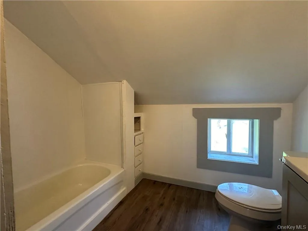 Full bathroom with vaulted ceiling, vanity, toilet, shower / bathing tub combination, and hardwood / wood-style floors Full bathroom with vaulted ceiling, vanity, toilet, shower / bathing tub combination, and hardwood / wood-style floors
