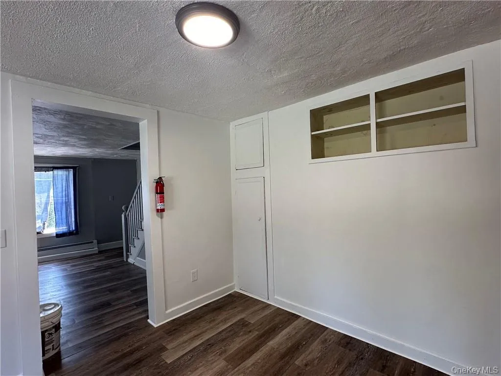 Unfurnished room featuring a textured ceiling, dark wood-type flooring, and a baseboard radiator Unfurnished room featuring a textured ceiling, dark wood-type flooring, and a baseboard radiator
