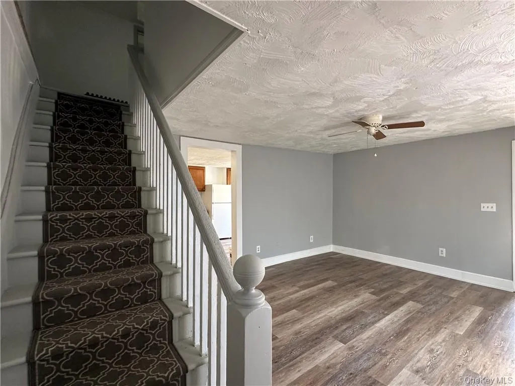 Stairway featuring a textured ceiling, hardwood / wood-style flooring, and ceiling fan Stairway featuring a textured ceiling, hardwood / wood-style flooring, and ceiling fan