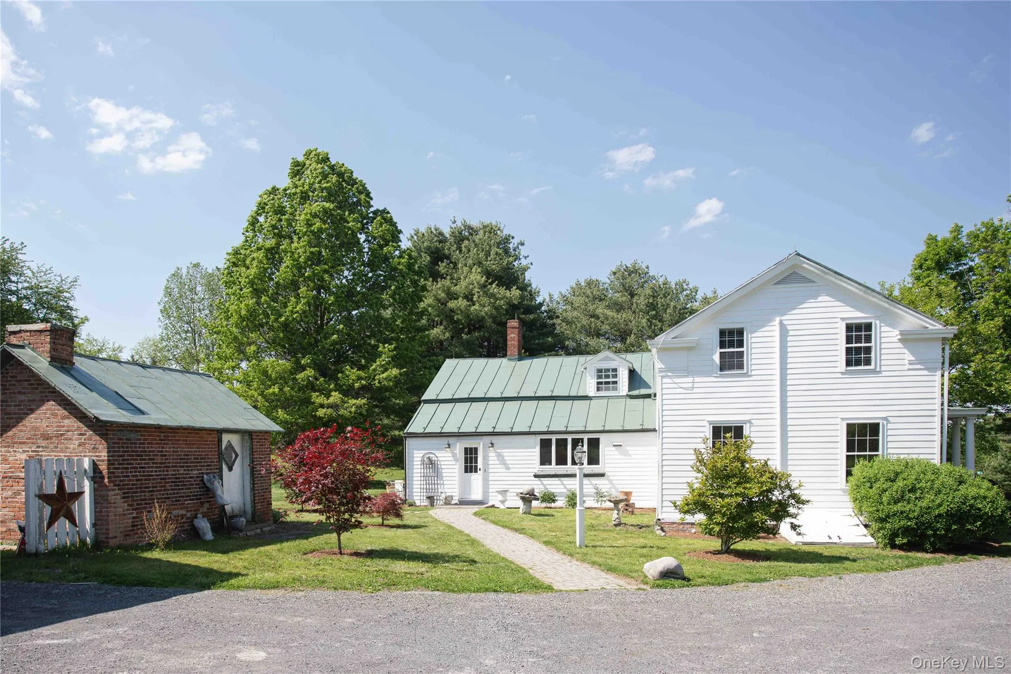 Main residence featuring a green metal roof, multiple windows, a landscaped side entry, and a red brick storage structure. Main residence featuring a green metal roof, multiple windows, a landscaped side entry, and a red brick storage structure.
