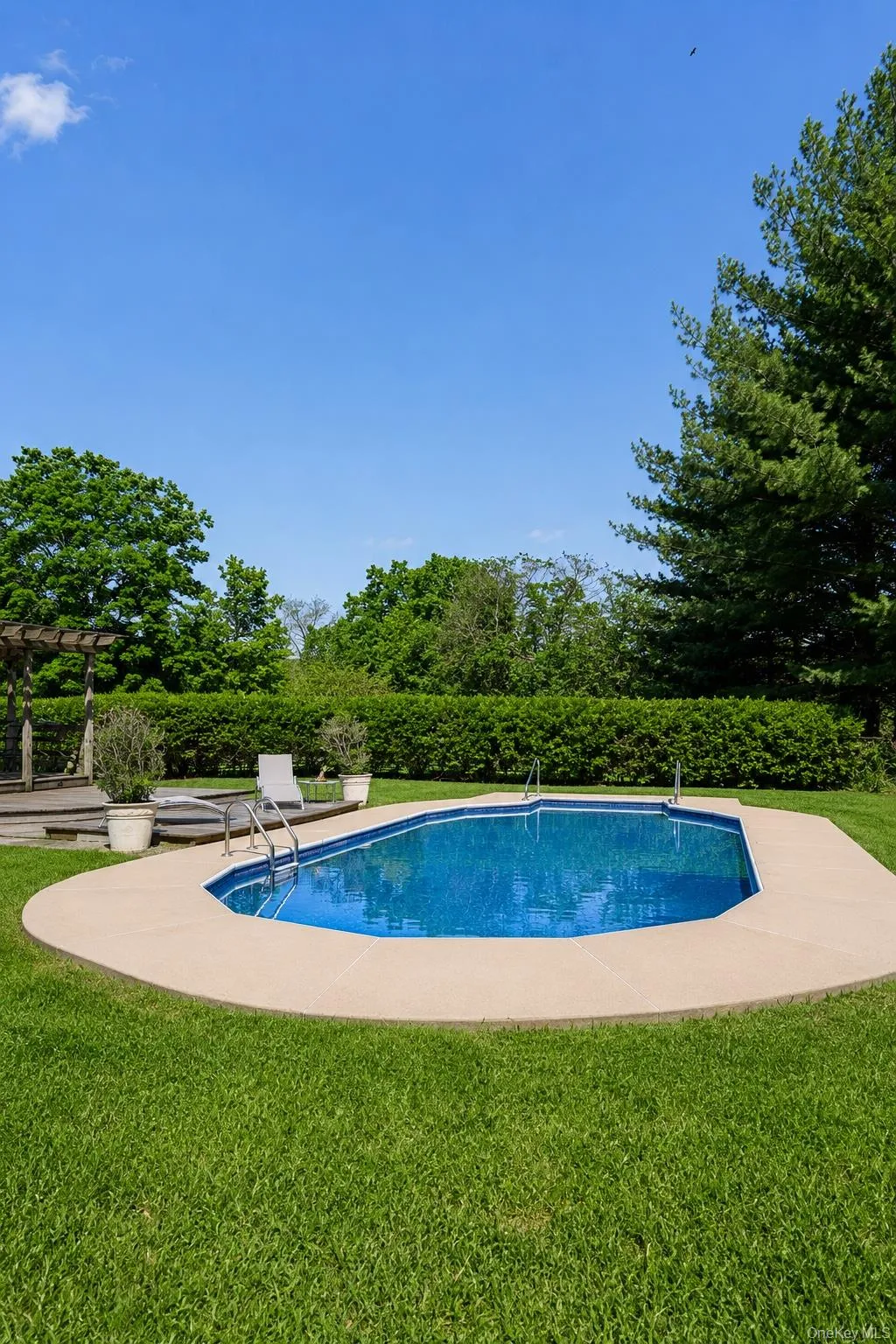 In-ground swimming pool featuring a concrete surround, metal entry ladders, and a surrounding lawn In-ground swimming pool featuring a concrete surround, metal entry ladders, and a surrounding lawn