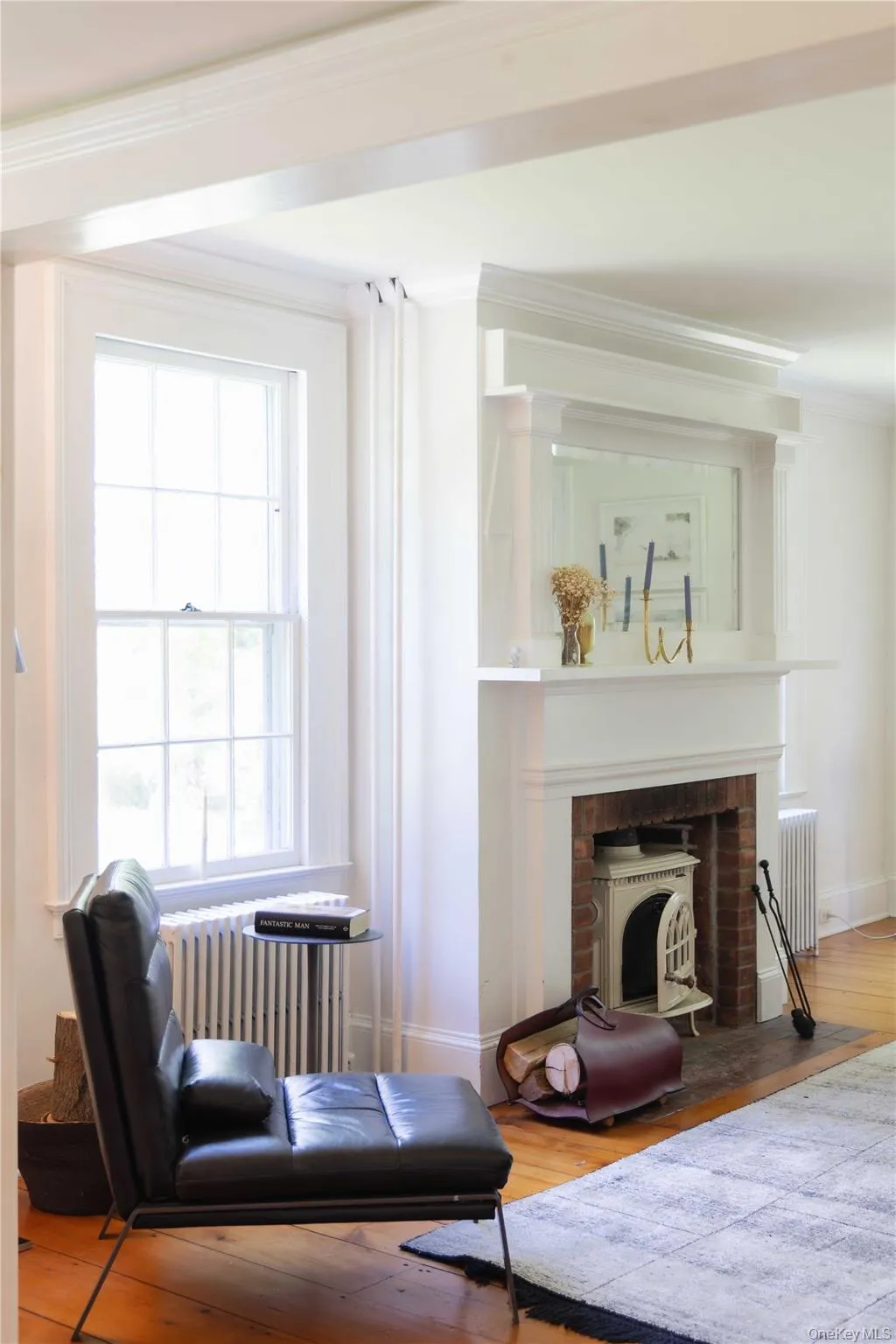 Hardwood flooring extending through the room, complemented by a fireplace with a detailed white mantel Hardwood flooring extending through the room, complemented by a fireplace with a detailed white mantel