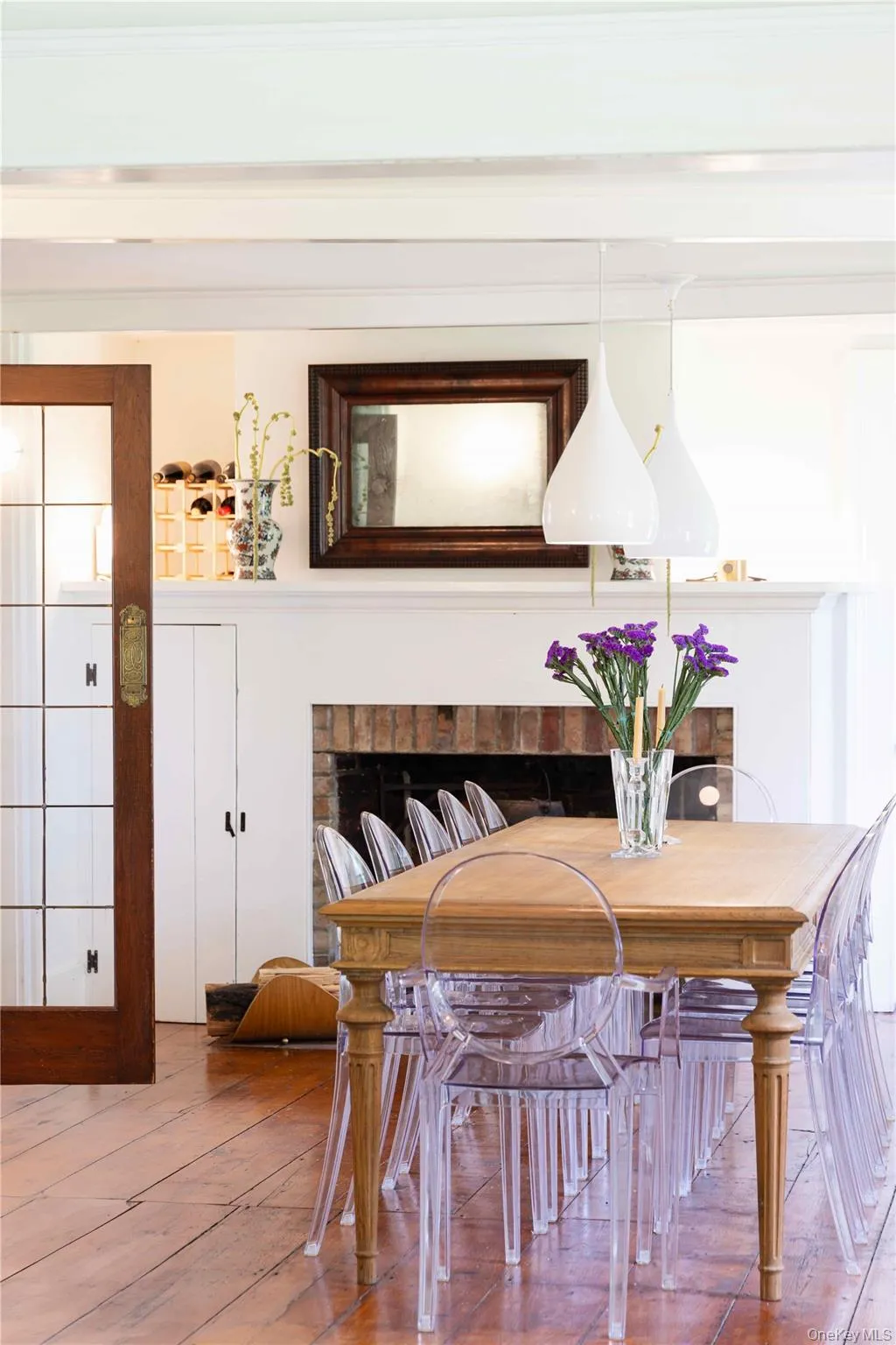 Dining area featuring wide plank wood flooring and a brick fireplace with a white mantel Dining area featuring wide plank wood flooring and a brick fireplace with a white mantel