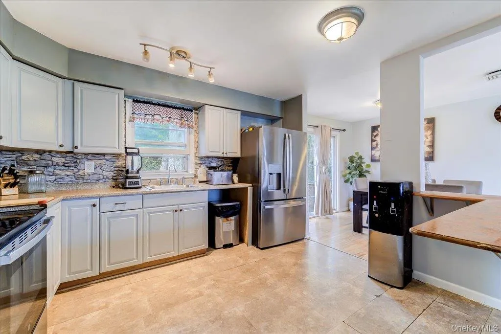 Kitchen featuring light cabinetry, a stone-look backsplash, light-toned countertops, and tile flooring Kitchen featuring light cabinetry, a stone-look backsplash, light-toned countertops, and tile flooring