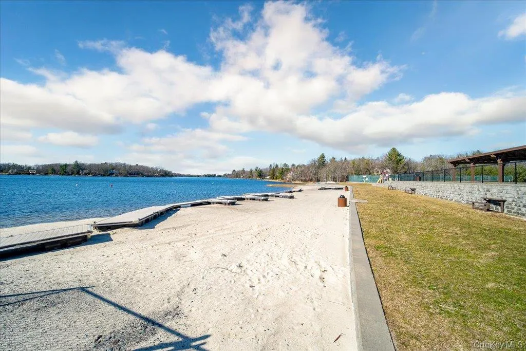 Extensive sandy beach with a wooden dock system, bordered by a grassy expanse and a stone retaining wall Extensive sandy beach with a wooden dock system, bordered by a grassy expanse and a stone retaining wall
