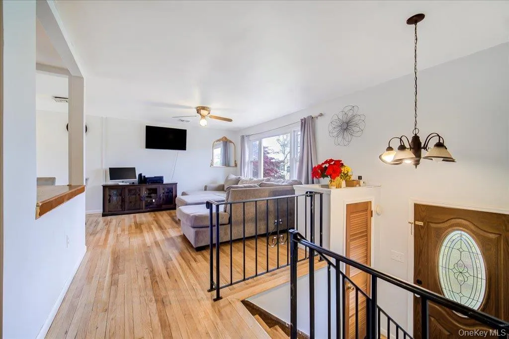 Open-concept living space featuring wood-finish flooring, a ceiling fan, and a chandelier lighting fixture Open-concept living space featuring wood-finish flooring, a ceiling fan, and a chandelier lighting fixture