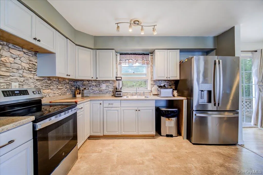 Kitchen featuring white cabinetry, stone-finish backsplash, stainless steel appliances, Kitchen featuring white cabinetry, stone-finish backsplash, stainless steel appliances,