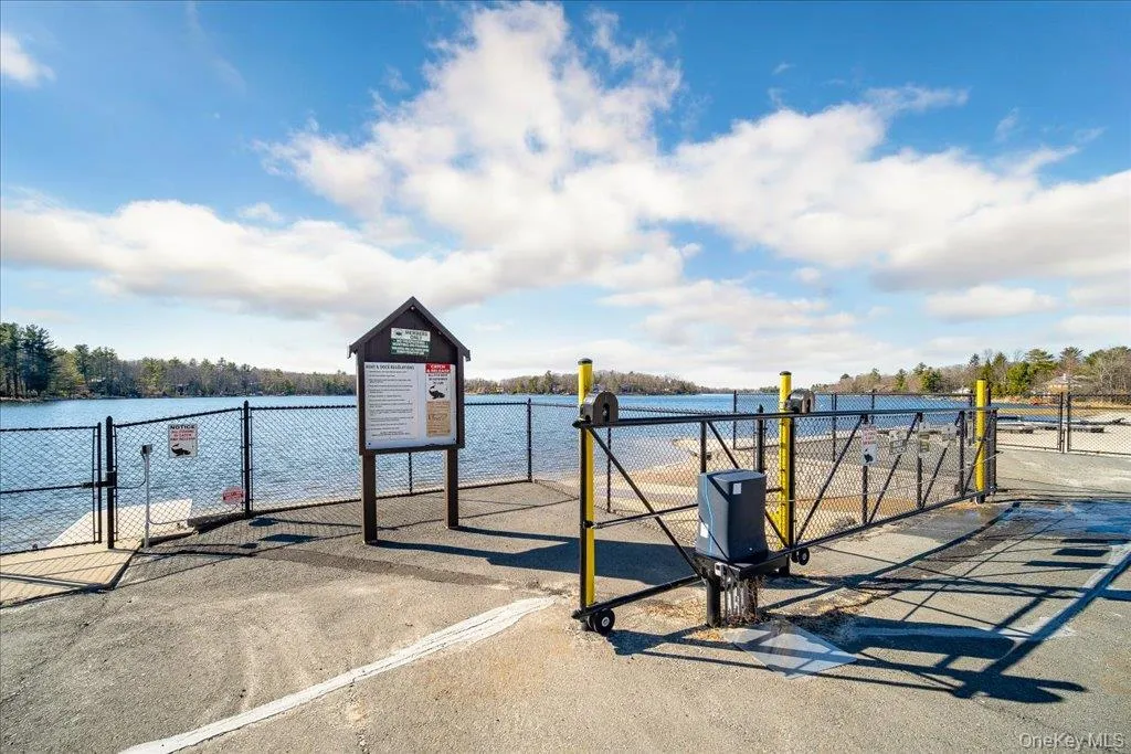 Waterfront access point featuring a paved approach, secure fencing, informational signage, a gated entry, and a visible body of water Waterfront access point featuring a paved approach, secure fencing, informational signage, a gated entry, and a visible body of water