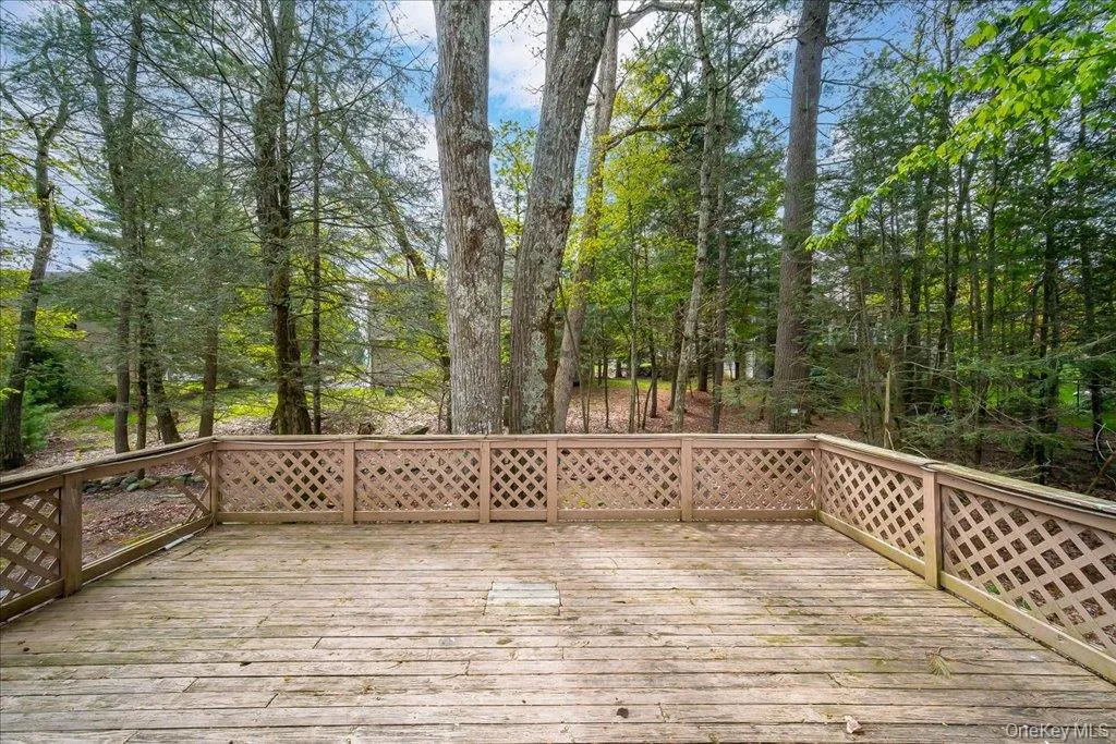 Expansive wooden deck with lattice railing, surrounded by mature trees and lush greenery Expansive wooden deck with lattice railing, surrounded by mature trees and lush greenery