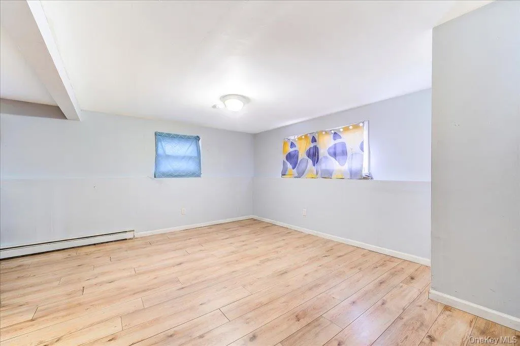 Spacious room featuring light wood-finish flooring, light gray walls, white baseboards, and a flush-mount ceiling light Spacious room featuring light wood-finish flooring, light gray walls, white baseboards, and a flush-mount ceiling light