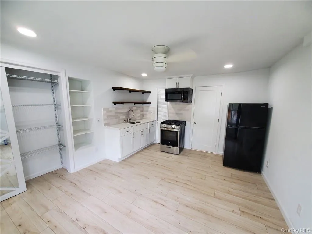 Kitchen with light hardwood / wood-style flooring, ceiling fan, white cabinetry, black appliances, and tasteful backsplash Kitchen with light hardwood / wood-style flooring, ceiling fan, white cabinetry, black appliances, and tasteful backsplash
