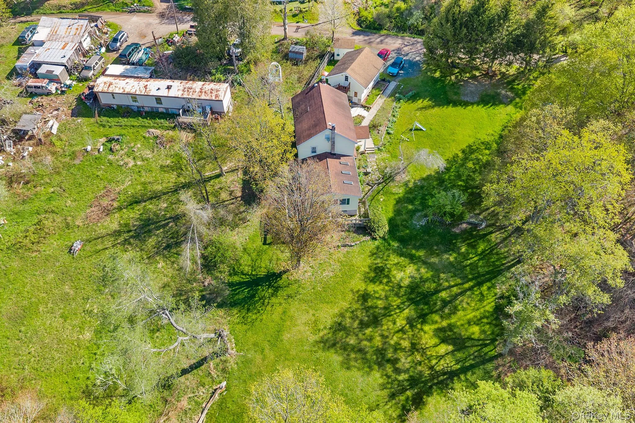 Spacious property featuring multiple structures, including a primary residence with a terracotta-colored roof and a separate structure with a metal roof Spacious property featuring multiple structures, including a primary residence with a terracotta-colored roof and a separate structure with a metal roof