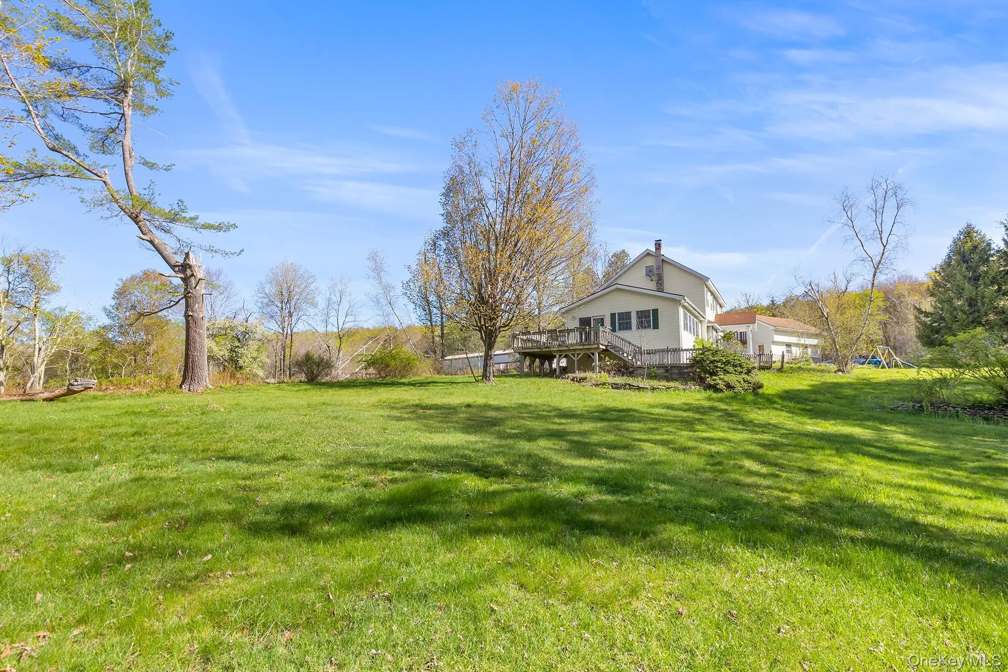 Expansive green lawn with mature trees and a two-story residence featuring a large deck Expansive green lawn with mature trees and a two-story residence featuring a large deck