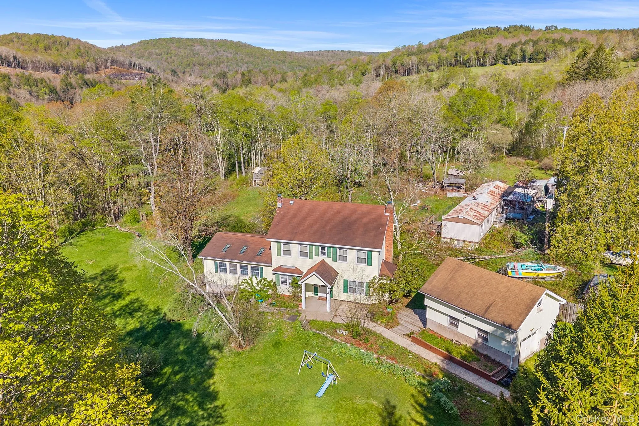 Expansive property featuring a two-story residence with a gabled roof and green shutters, complemented by a detached garage structure Expansive property featuring a two-story residence with a gabled roof and green shutters, complemented by a detached garage structure
