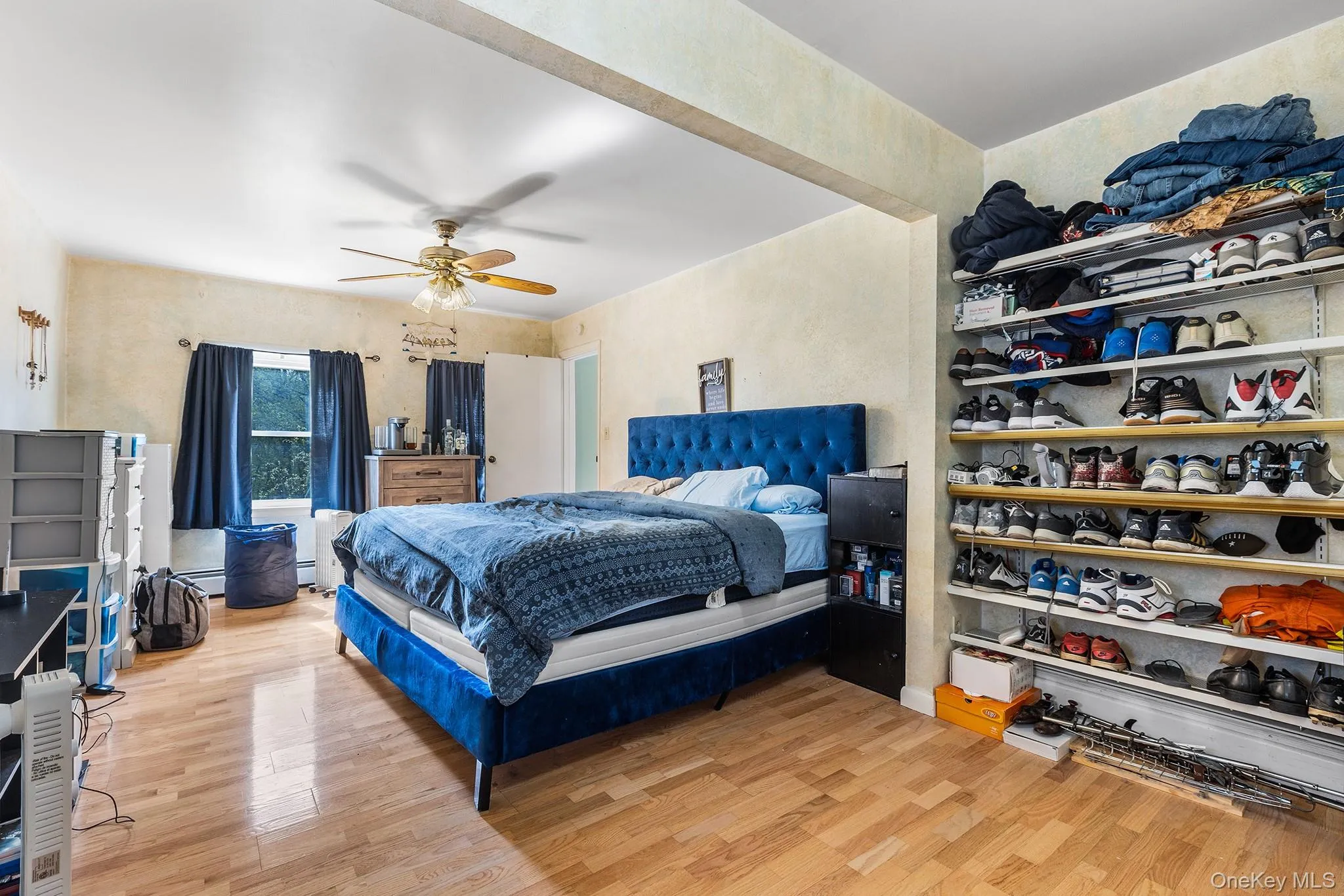 Bedroom featuring wood-finish flooring, a ceiling fan with light fixture, and windows with dark window treatments Bedroom featuring wood-finish flooring, a ceiling fan with light fixture, and windows with dark window treatments