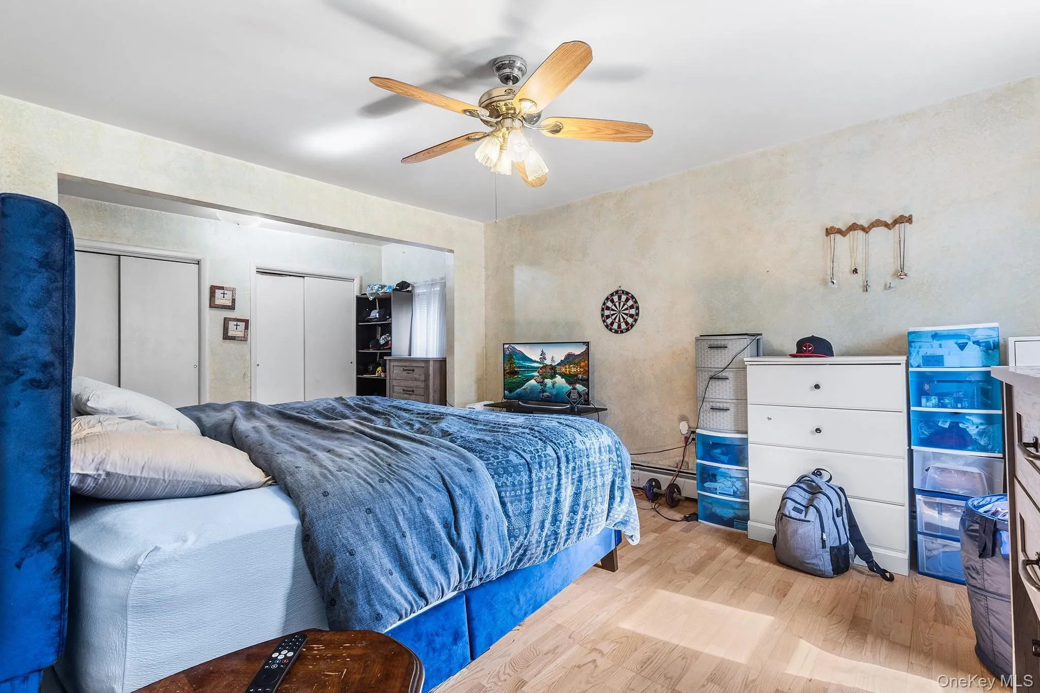Room featuring wood-finish flooring, a ceiling fan with integrated lighting, and multiple sliding door closets for ample storage Room featuring wood-finish flooring, a ceiling fan with integrated lighting, and multiple sliding door closets for ample storage