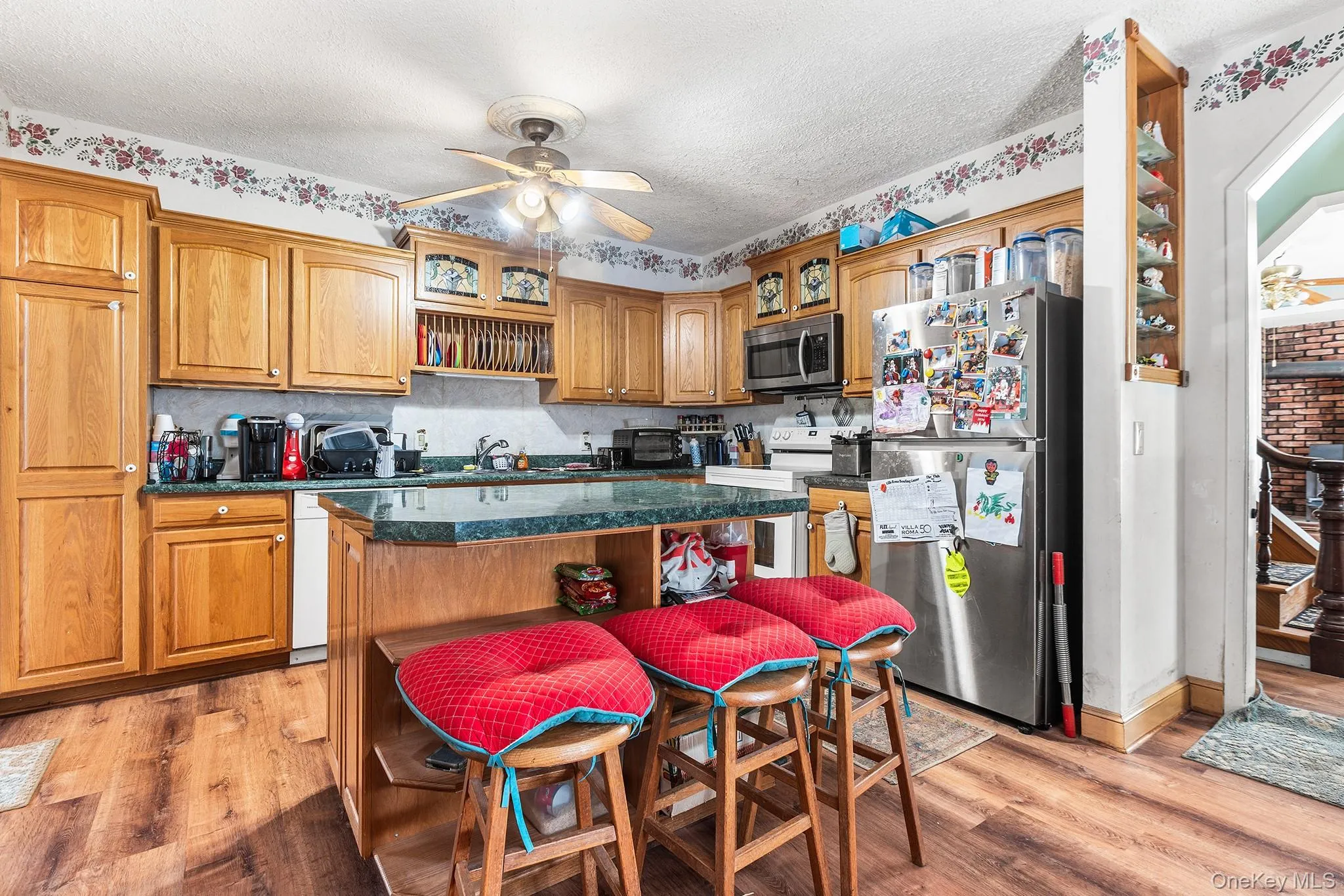 Kitchen featuring wood-finish flooring, wood cabinetry, a center island with countertop seating, and a stainless steel refrigerator Kitchen featuring wood-finish flooring, wood cabinetry, a center island with countertop seating, and a stainless steel refrigerator