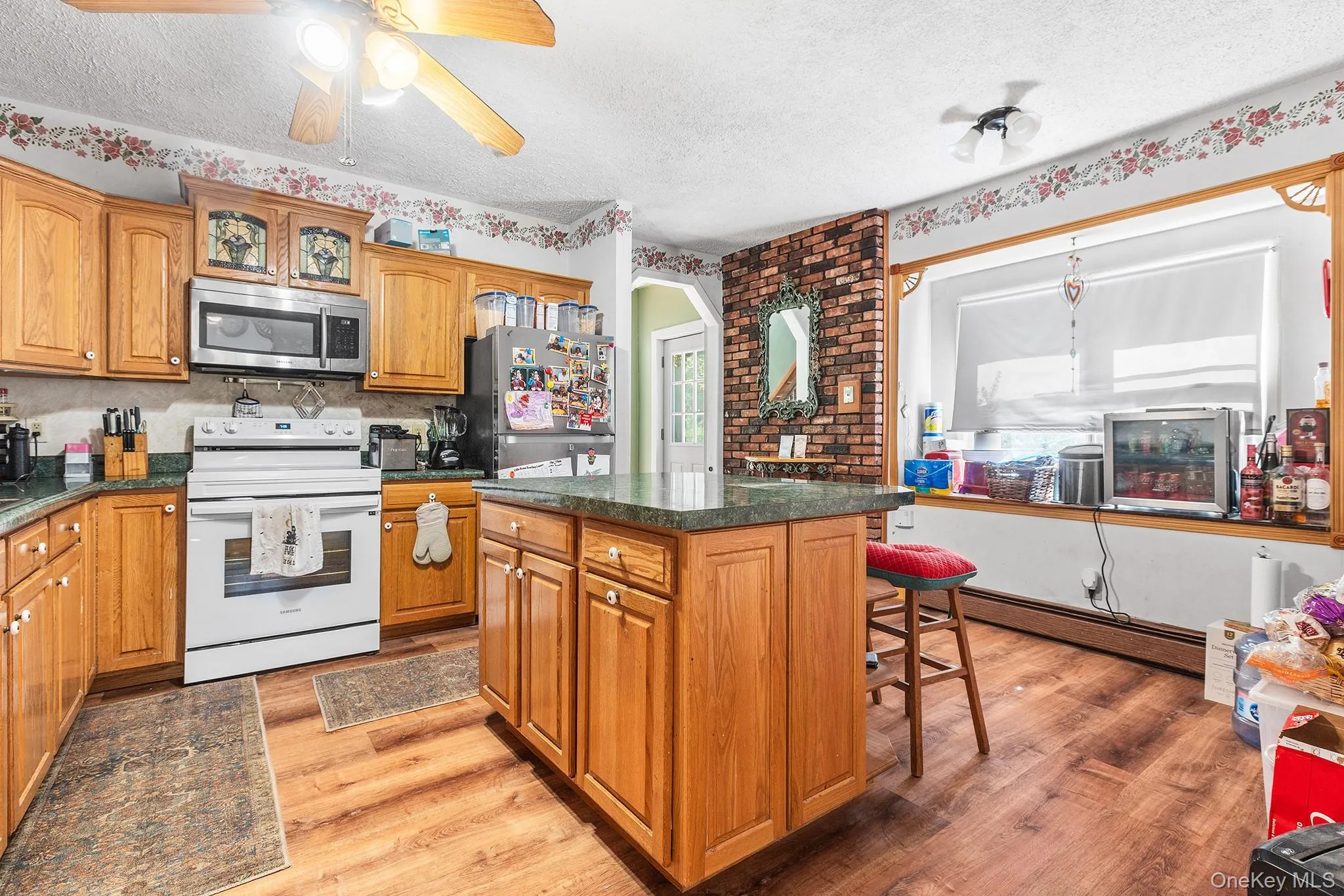 Kitchen featuring wood cabinetry with brass hardware, a central island with countertop, stainless steel microwave, and wood-finish flooring Kitchen featuring wood cabinetry with brass hardware, a central island with countertop, stainless steel microwave, and wood-finish flooring