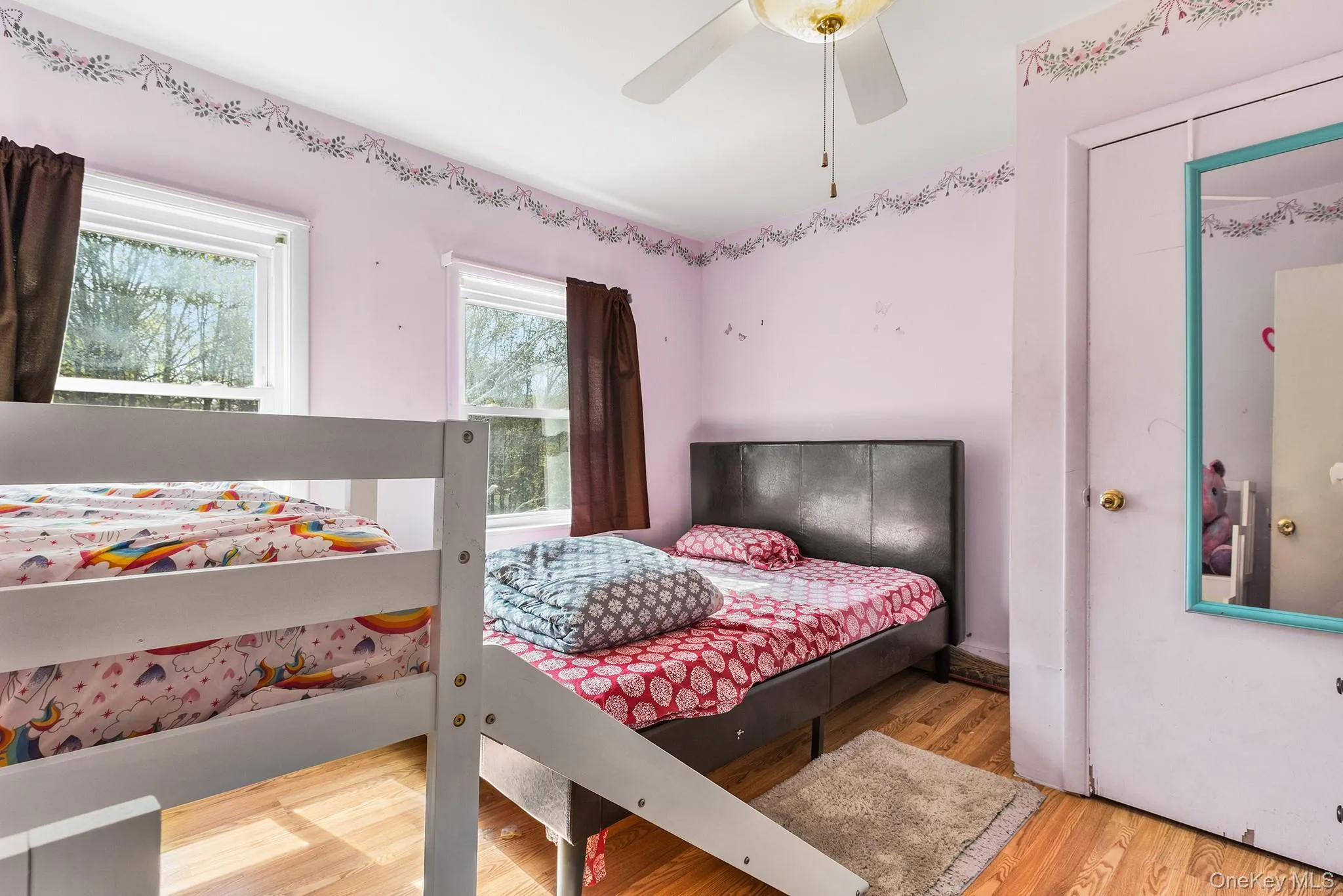 Light-filled room featuring two windows with white trim, wood-finish flooring, and a ceiling fan with integrated lighting Light-filled room featuring two windows with white trim, wood-finish flooring, and a ceiling fan with integrated lighting