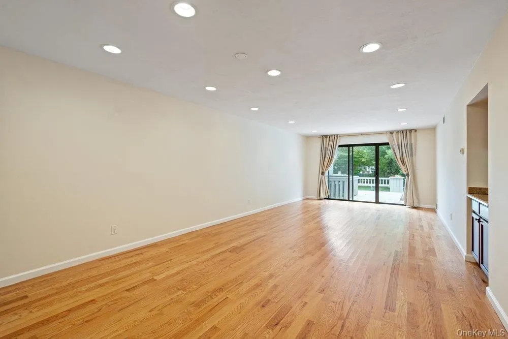 Spacious room featuring wood-finish flooring, recessed lighting, and a sliding glass door leading to a deck Spacious room featuring wood-finish flooring, recessed lighting, and a sliding glass door leading to a deck