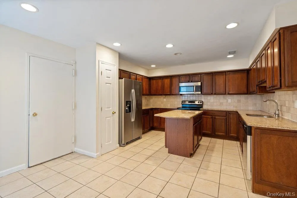 Kitchen featuring rich wood cabinetry, stainless steel appliances, a center island with countertop, tile flooring, and recessed lighting Kitchen featuring rich wood cabinetry, stainless steel appliances, a center island with countertop, tile flooring, and recessed lighting