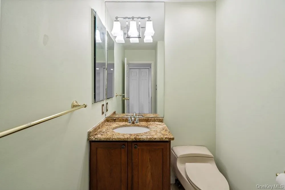Vanity with a granite countertop and an integrated sink, wood-finish cabinetry, polished chrome faucet, rectangular mirror, and a four-light vanity fixture Vanity with a granite countertop and an integrated sink, wood-finish cabinetry, polished chrome faucet, rectangular mirror, and a four-light vanity fixture