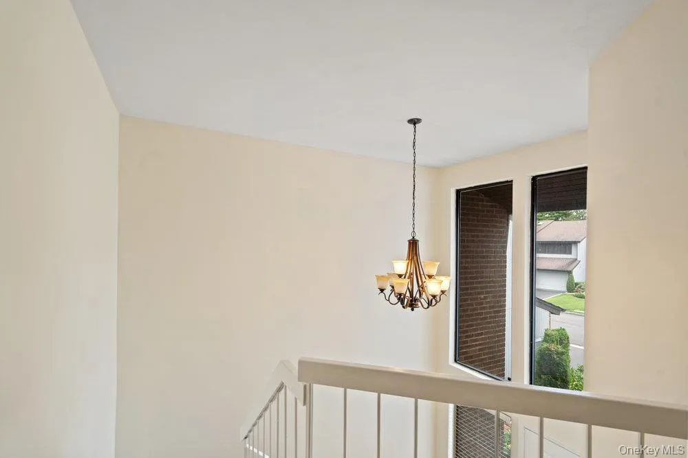 Stairwell featuring a multi-light chandelier, two vertical windows with dark framing, and a light-toned railing Stairwell featuring a multi-light chandelier, two vertical windows with dark framing, and a light-toned railing