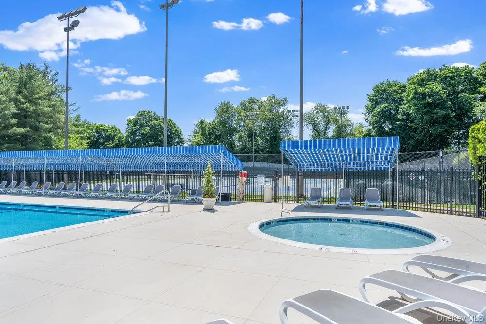 Outdoor swimming pool with integrated hot tub, extensive concrete decking, and a shaded lounge area featuring blue and white striped awnings Outdoor swimming pool with integrated hot tub, extensive concrete decking, and a shaded lounge area featuring blue and white striped awnings