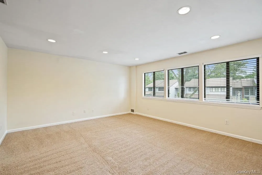 Spacious room featuring neutral carpeting, a series of three large windows with horizontal blinds, and recessed lighting fixtures Spacious room featuring neutral carpeting, a series of three large windows with horizontal blinds, and recessed lighting fixtures