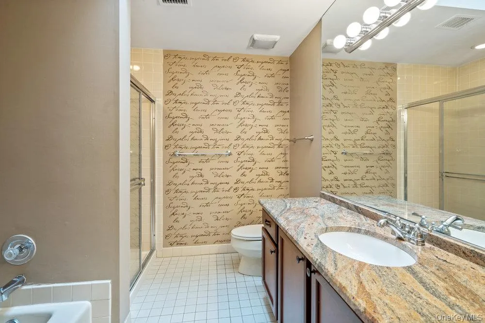 Bathroom featuring a vanity with an undermount sink, a stone-finish countertop, and dark wood-finish cabinetry Bathroom featuring a vanity with an undermount sink, a stone-finish countertop, and dark wood-finish cabinetry