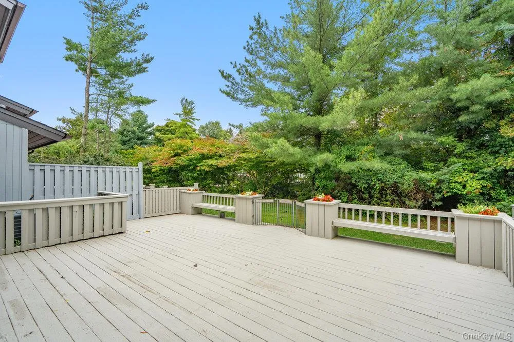 Expansive outdoor deck featuring wood-finish flooring, built-in benches, integrated planter boxes, a privacy fence, and a gate providing access to a treed perimeter Expansive outdoor deck featuring wood-finish flooring, built-in benches, integrated planter boxes, a privacy fence, and a gate providing access to a treed perimeter