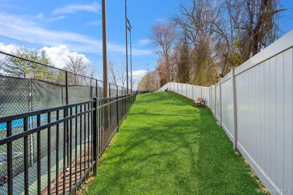 Manicured lawn area bordered by a black metal fence and a white privacy fence Manicured lawn area bordered by a black metal fence and a white privacy fence