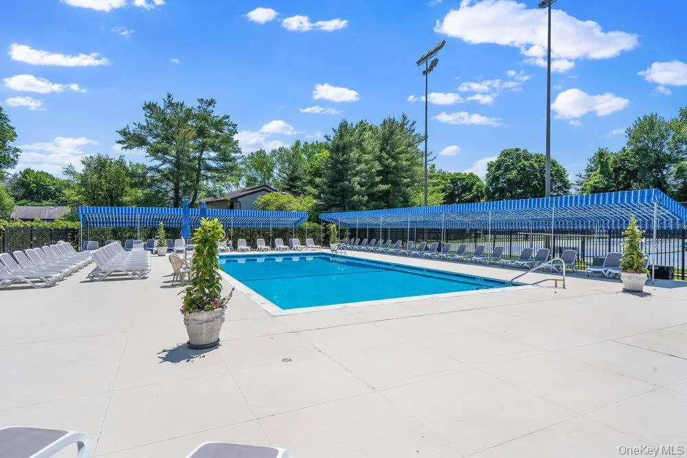 Expansive outdoor swimming pool featuring a large paved deck, perimeter fencing, and shaded lounge areas with striped canopies Expansive outdoor swimming pool featuring a large paved deck, perimeter fencing, and shaded lounge areas with striped canopies