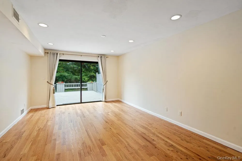 Spacious room featuring wood-finish flooring, recessed lighting, and a sliding glass door opening to an outdoor deck with a railing Spacious room featuring wood-finish flooring, recessed lighting, and a sliding glass door opening to an outdoor deck with a railing