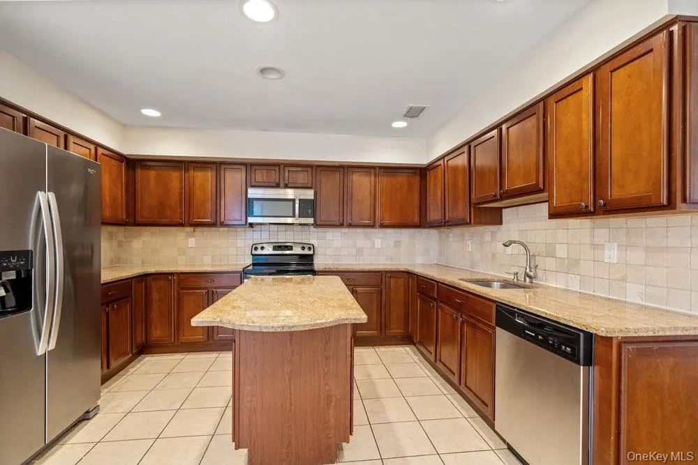 Kitchen featuring wood-finish cabinetry, light-toned countertops, stainless steel appliances, a center island, and recessed lighting Kitchen featuring wood-finish cabinetry, light-toned countertops, stainless steel appliances, a center island, and recessed lighting