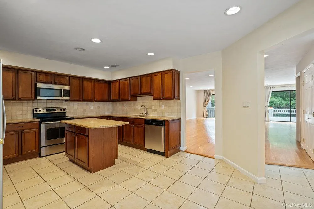 Kitchen featuring dark wood cabinetry, stainless steel appliances, a center island with countertop, and tile flooring Kitchen featuring dark wood cabinetry, stainless steel appliances, a center island with countertop, and tile flooring