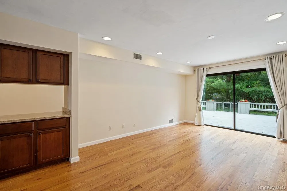 Spacious room featuring wood-finish flooring, recessed lighting, and a built-in cabinetry unit with a light-toned countertop Spacious room featuring wood-finish flooring, recessed lighting, and a built-in cabinetry unit with a light-toned countertop