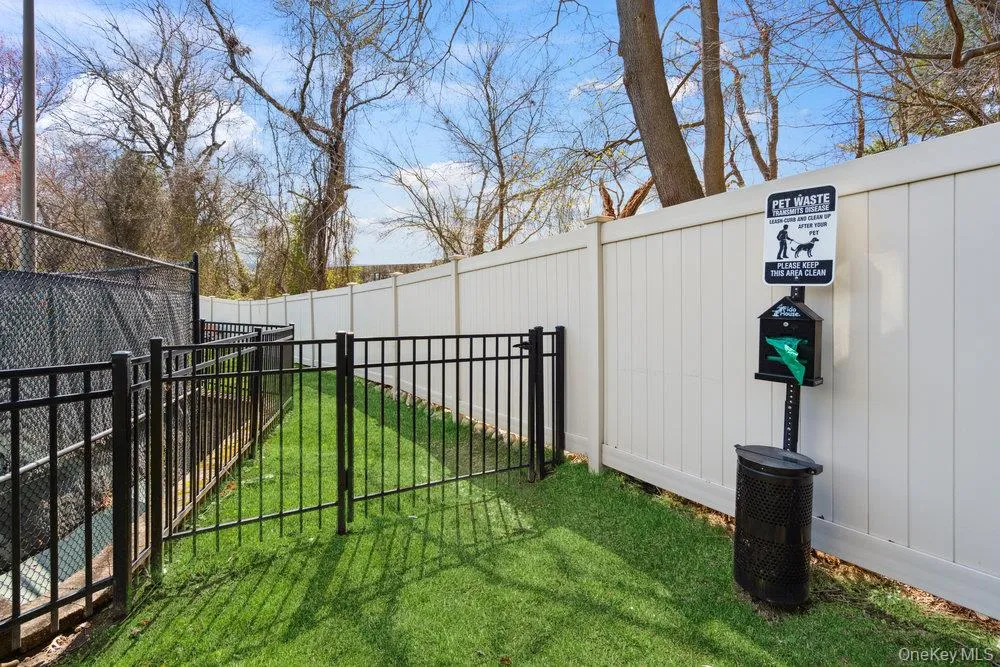 Enclosed pet area featuring a black metal fence, a white privacy fence, and a manicured lawn Enclosed pet area featuring a black metal fence, a white privacy fence, and a manicured lawn