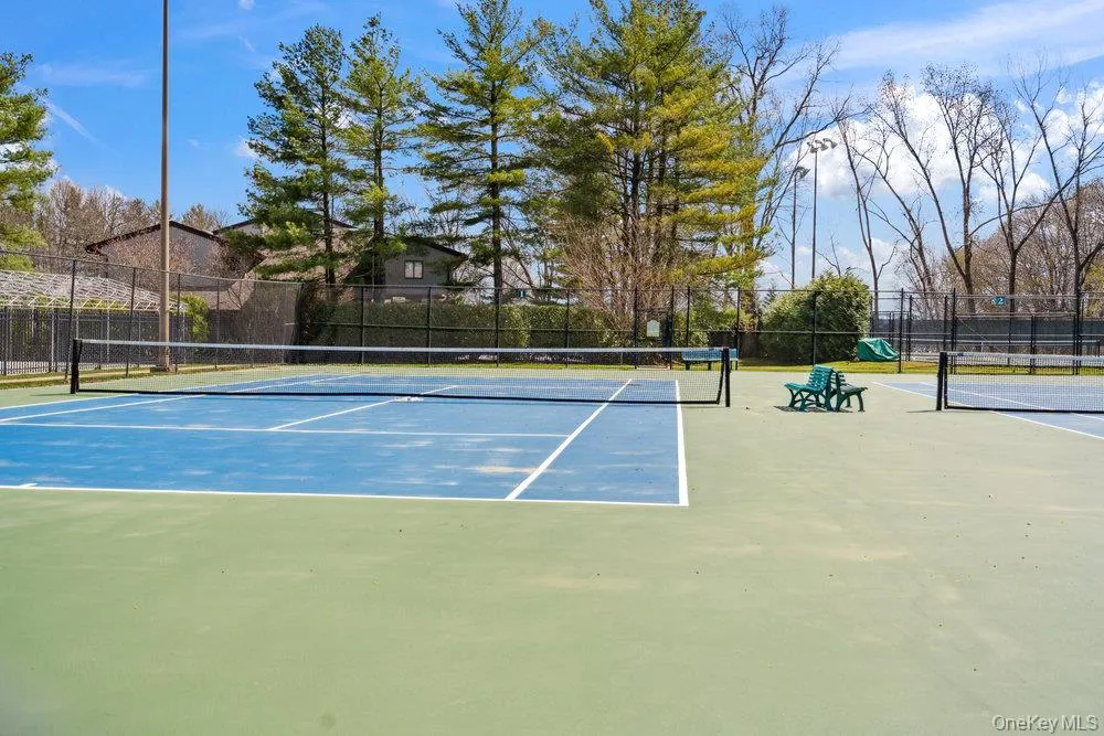 Hard surface tennis courts featuring blue and green playing areas, perimeter fencing, and mature trees Hard surface tennis courts featuring blue and green playing areas, perimeter fencing, and mature trees