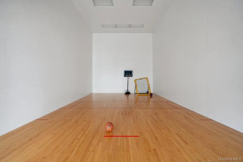 Indoor recreational space featuring light wood-finish flooring with red court lines, white walls, and recessed ceiling lighting Indoor recreational space featuring light wood-finish flooring with red court lines, white walls, and recessed ceiling lighting