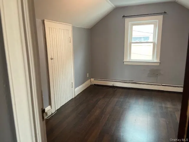 Bonus room featuring dark hardwood / wood-style flooring, vaulted ceiling, and a baseboard heating unit Bonus room featuring dark hardwood / wood-style flooring, vaulted ceiling, and a baseboard heating unit