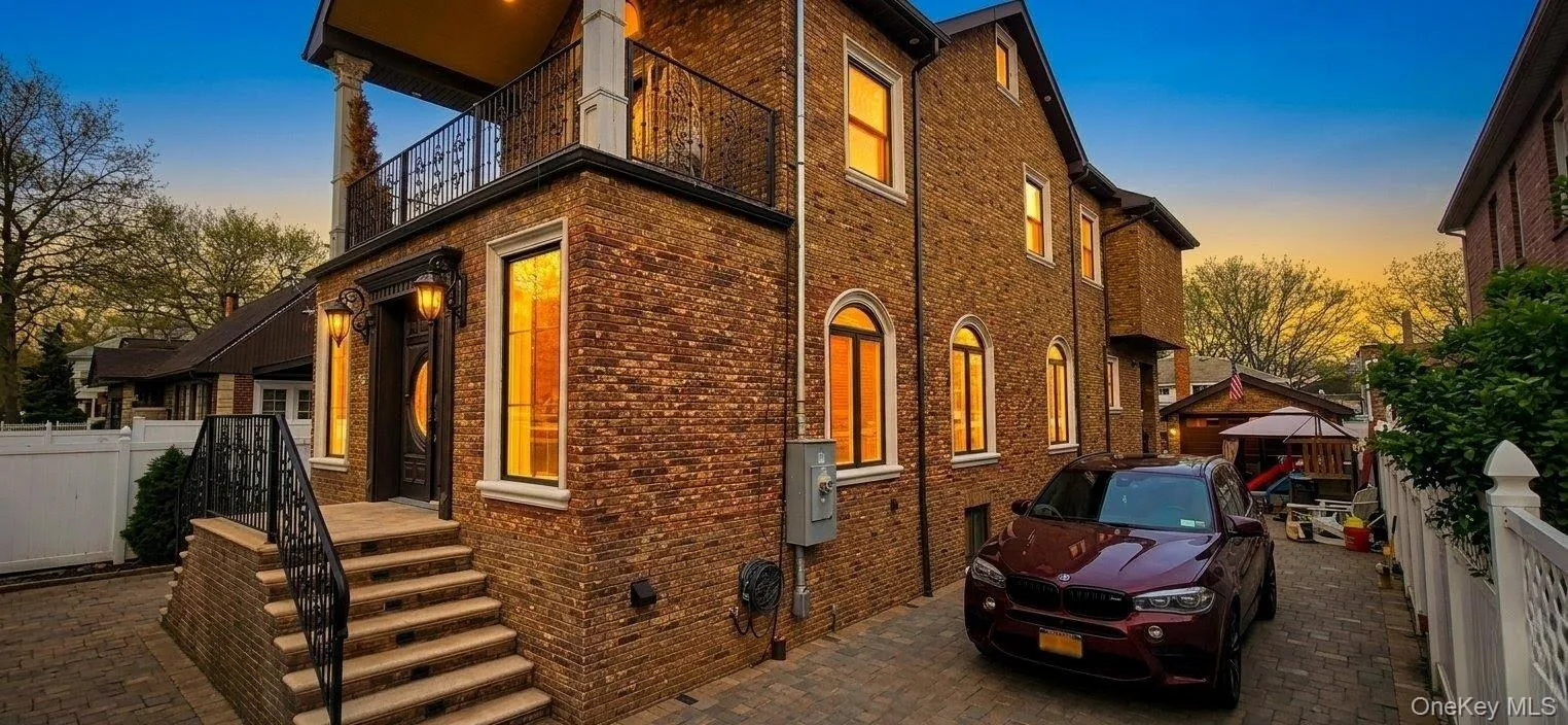 Brick facade residence featuring a paver driveway, wrought iron balcony railing, and exterior sconce lighting. A.I Enchanced Brick facade residence featuring a paver driveway, wrought iron balcony railing, and exterior sconce lighting. A.I Enchanced
