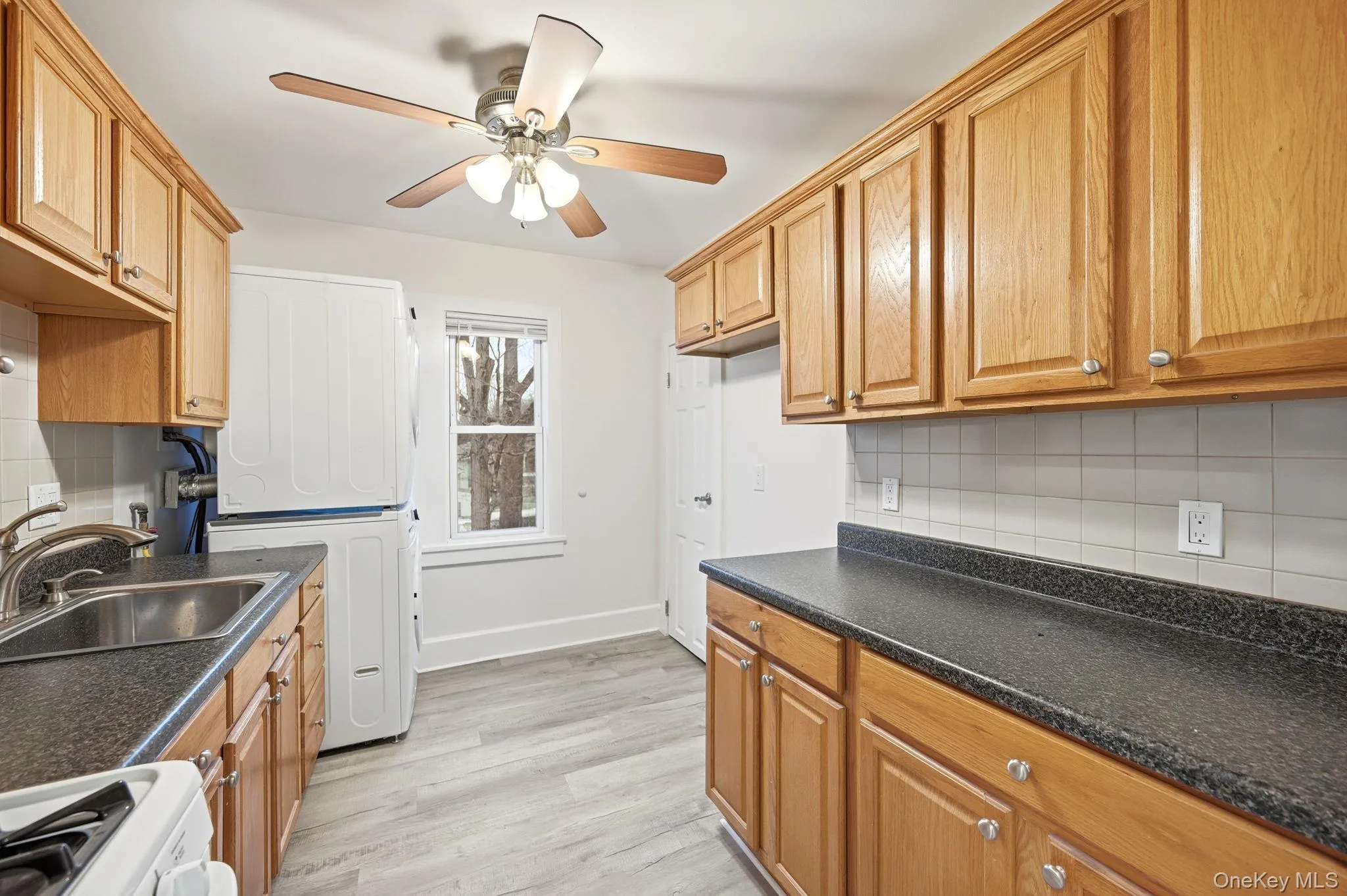 Kitchen with tasteful backsplash, dark countertops, and stacked washing machine and dryer Kitchen with tasteful backsplash, dark countertops, and stacked washing machine and dryer
