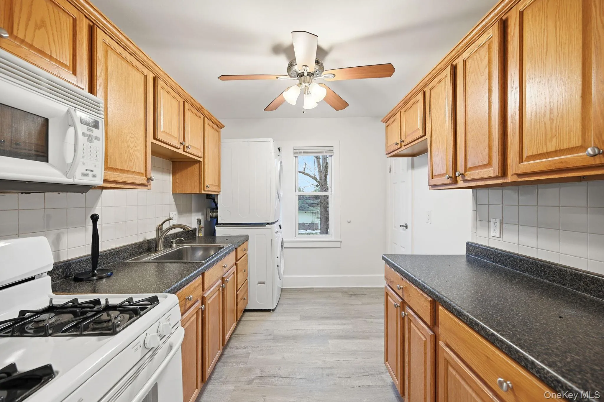 Kitchen with white appliances, backsplash, dark countertops, and ceiling fan Kitchen with white appliances, backsplash, dark countertops, and ceiling fan
