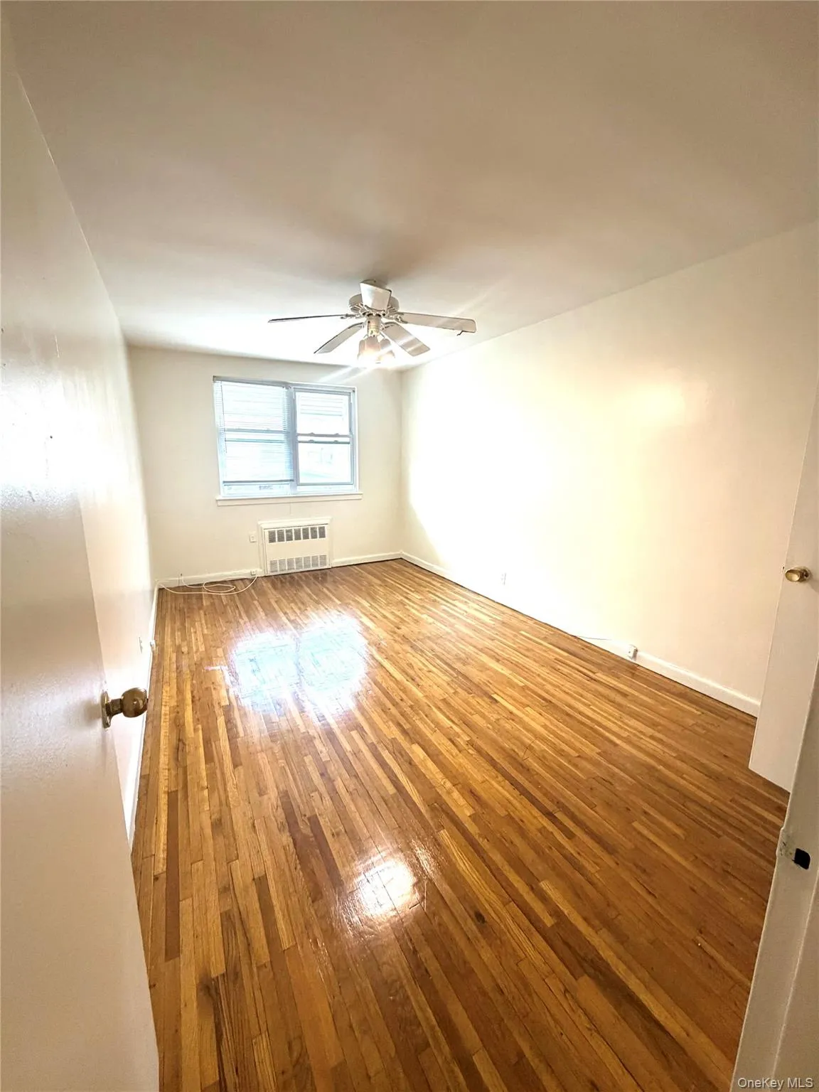 Second bedroom with Hardwood flooring throughout featuring a ceiling fan, window, and wall-mounted radiator Second bedroom with Hardwood flooring throughout featuring a ceiling fan, window, and wall-mounted radiator