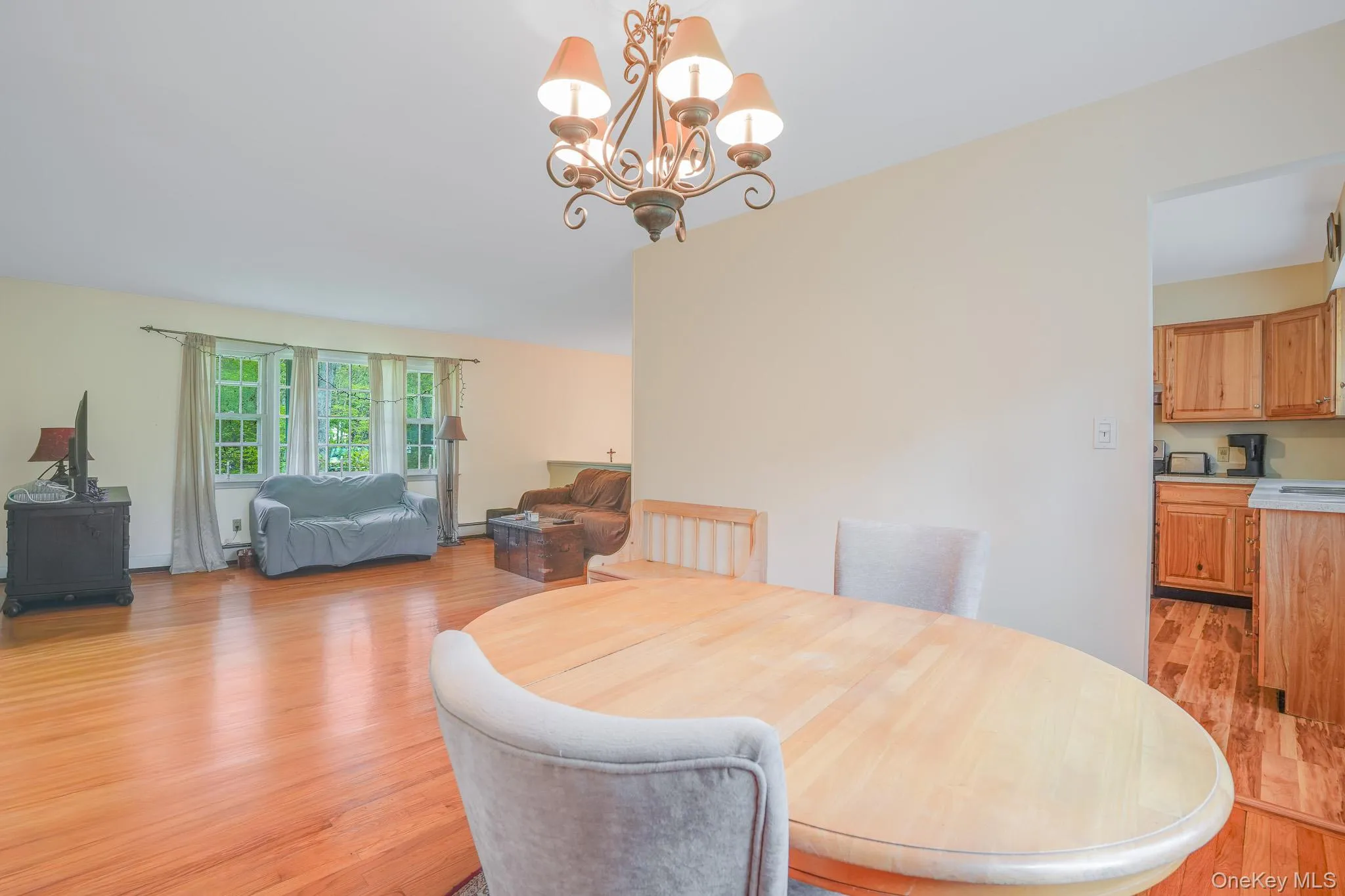 Open-concept interior featuring wood-finish flooring, a decorative chandelier, and a bay window Open-concept interior featuring wood-finish flooring, a decorative chandelier, and a bay window