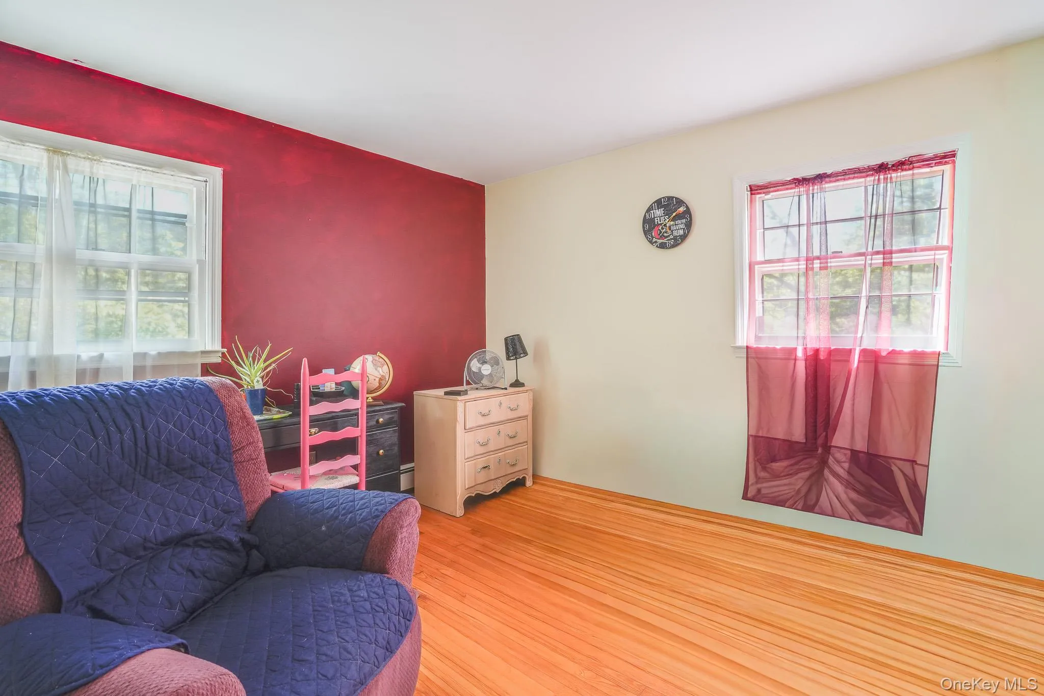 Room featuring wood-finish flooring, white trim, and light-toned walls with one accent wall Room featuring wood-finish flooring, white trim, and light-toned walls with one accent wall